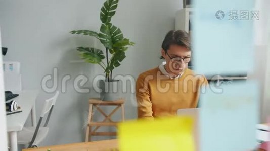 男性办公室工作人员在玻璃板后面使用笔记本电脑，上面有明亮的贴纸视频