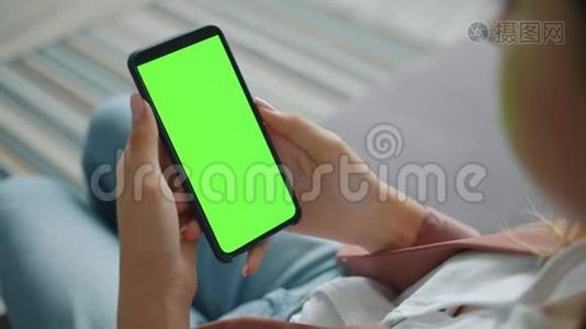 女性手拿着现代智能手机，手里拿着空白绿色屏幕视频