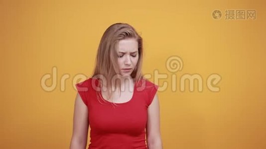 年轻的金发女孩穿着红色t恤，在橙色的背景下表现出情绪视频