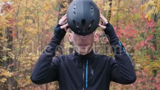 在秋季公园，一个穿着黑色运动服的年轻迷人的白人男子戴上黑色自行车头盔和运动眼镜。米视频
