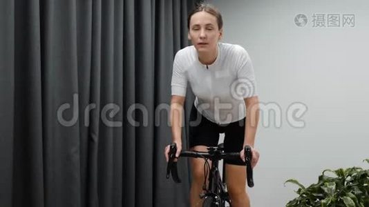 女人骑着固定的自行车在室内骑自行车。 专注女性在室内智能自行车训练器上进行健身训练，视频