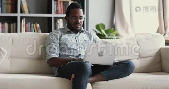 严肃的非洲年轻人手提电脑坐在沙发上视频