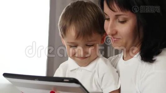 幸福的母亲和儿子的肖像。 母亲在平板电脑上使用一个孩子的发育申请视频