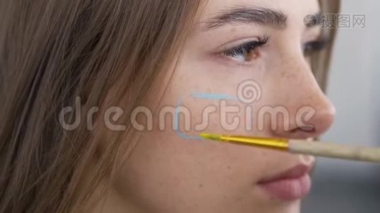 一个年轻漂亮女人的详细肖像。 艺术家用小软刷子在女孩`脸上作画。 身体艺术视频