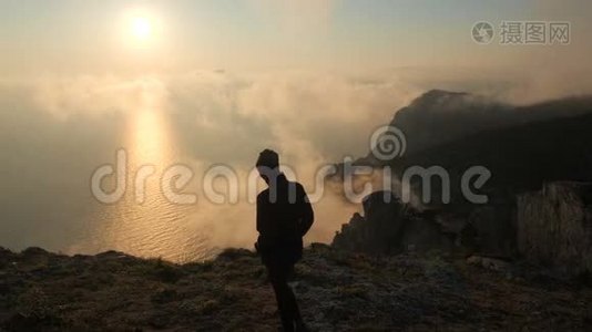 一位年轻女子沿着海边的悬崖边散步，从高处观看美丽的戏剧性日落视频