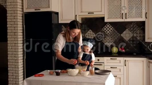 一个母亲和一个女儿一起准备面团，他们把鸡蛋打碎成一个碗。视频