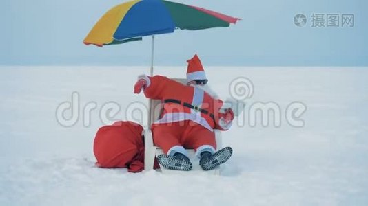 圣诞老人坐在一张带着平板电脑的躺椅上，他的伞被吹走了视频