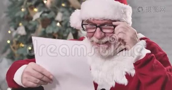 戴眼镜的圣诞老人在看书，微笑着。 穿着圣诞服装坐在后台的老白种人视频