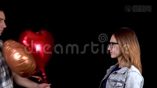 一个年轻人给一个年轻的女人心形气球。 男人和女人在黑色背景上接吻。 情人节`是视频