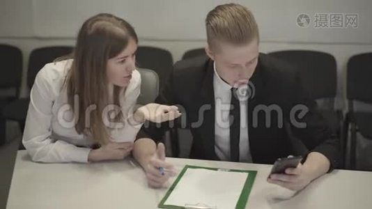 年轻的高加索男人和女人看着智能手机屏幕说话。 讨论商业想法的同事视频