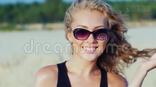 一个年轻迷人的女人微笑着，看着镜头，在海滩上摆姿势的肖像视频