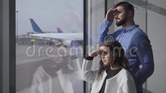 侧面观察特写白人男子和小女孩看着玻璃机场窗口在跑道。 父亲和视频