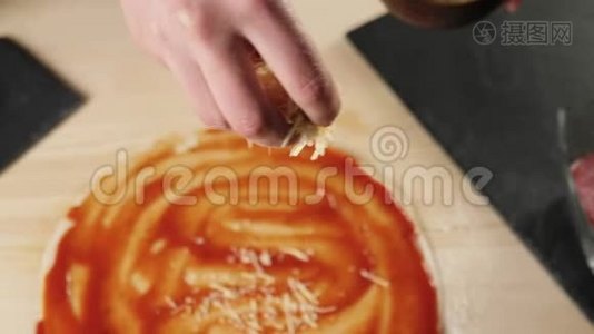 专业厨师将磨碎的奶酪倒入一个披萨基地，桌子上放着番茄酱，上面装饰着披萨配料视频