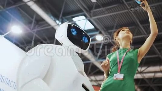 一个漂亮的女孩用机器人自拍。 机器人跟女人调情。 现代机器人技术。 机器人看着视频