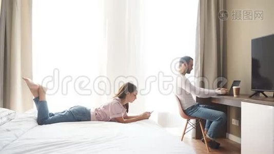 年轻漂亮的夫妇在卧室里休息，男人坐在电脑前，在家工作视频