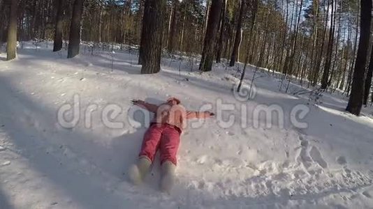一个穿着桃色夹克和粉红色暖裤的女孩躺在雪堆里，手举起来。 在毡靴的腿上。 清澈的冰霜视频