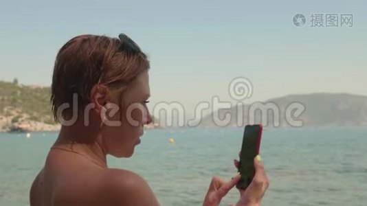 旅游妇女拍摄海洋到手机。 用智能手机拍摄海上某物的成年女性晒黑视频