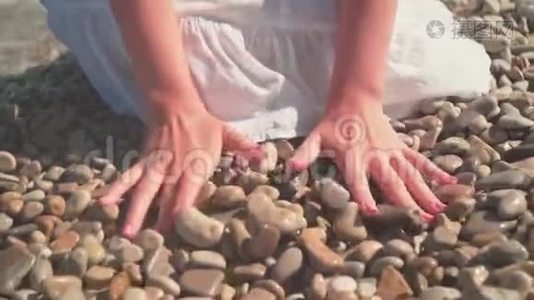 一个女人的特写`她的手捡起一块石头，然后把它从海滩上的手掌上扔了出来。视频