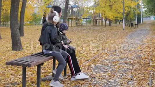 一位年轻的母亲，两个孩子坐在秋天公园的长凳上。 友好的家庭观念..视频
