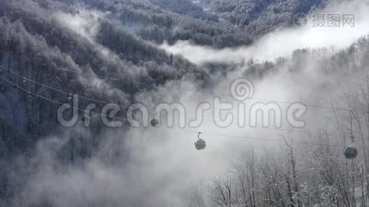 滑雪电梯在低地白色雪山云林上移动。 提供带滑雪者和滑雪板的滑雪缆车视频