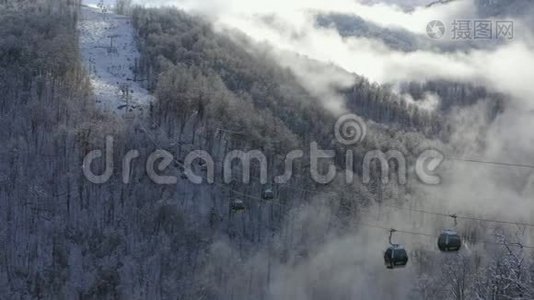 滑雪电梯在低地白色雪山云林上移动。 提供带滑雪者和滑雪板的滑雪缆车视频