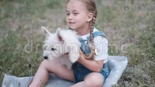 小金发女孩抱着西高地白梗小狗在公园。视频