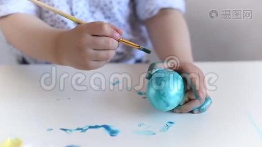 一个小小孩用画笔在桌子上画一个蓝色的复活节彩蛋视频