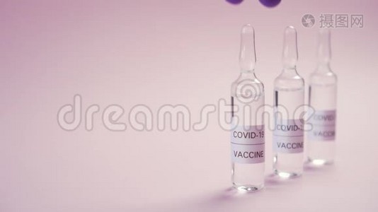冠状病毒疫苗。 一只手戴着蓝色防护医疗手套，在粉红色的表面上拿起安瓿视频