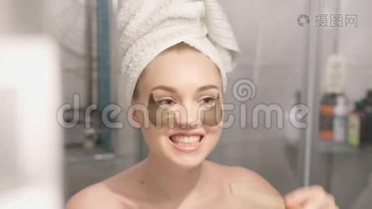 一张美丽的年轻女子的肖像，穿着浴袍和毛巾站在浴室里，在浴室下面敲击补片视频