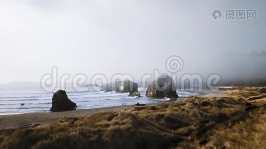 无人机摄像机正在接近一对夫妇，他们沿着海岸行走，巨大的石头从水中突出出来视频