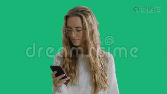 戴着时髦眼镜的漂亮年轻女人拿着智能手机，用智能手机，在绿色屏幕上微笑视频