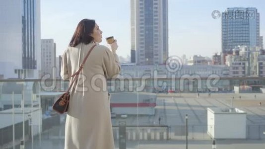 年轻的白种人女人喝咖啡和看城市街道的后景。 穿着优雅外套的成功女人视频