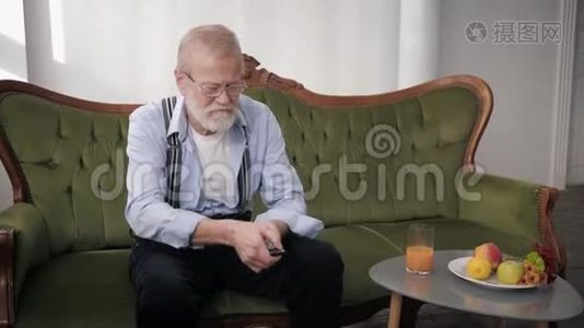 祖父戴着眼镜，留着胡子，背部疼痛，双手抓着下背部，坐在沙发上视频