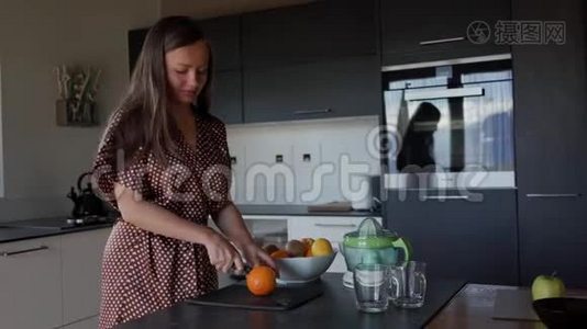 穿着棕色睡衣的微笑女人在厨房用刀子切橘子，用来做新鲜果汁。 一般视频