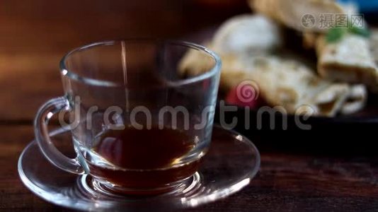早餐有煎饼和茶。把热茶倒进一个透明的杯子里。在木制背景上。视频