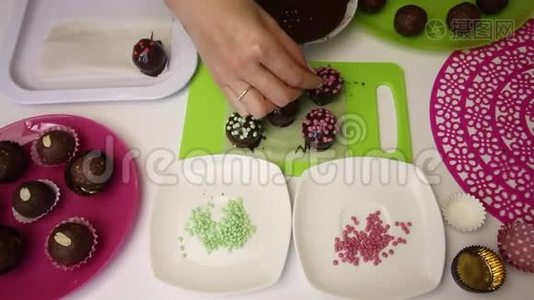 一个女人用洒满巧克力球装饰。 做一个土豆蛋糕。 盘子旁边有蛋糕、液体巧克力和视频