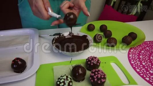 一个女人把一个巧克力海绵球放在表面。 做土豆蛋糕。 盘子旁边有蛋糕、液体巧克力和视频