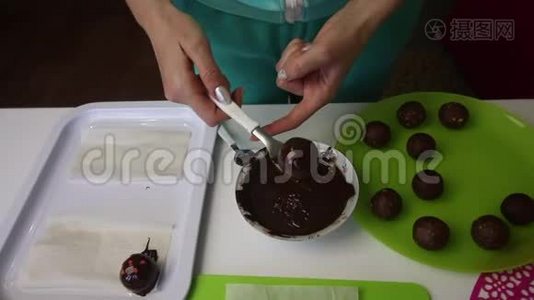 一个女人把一个巧克力海绵球放在表面。 做一个土豆蛋糕。 盘子旁边有蛋糕、液体巧克力和视频