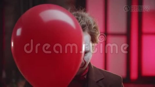 一个可怕的小丑，脸上有裂纹的油漆，从红色气球里偷看，还有令人毛骨悚然的微笑-邪恶的小丑概念视频