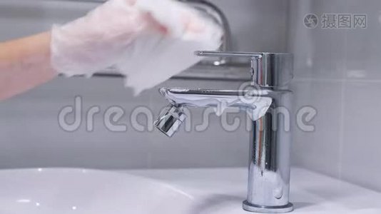 女人`戴手套的手用洗涤剂清洗浴室里的不锈钢水龙头。 检疫卫生。 Covid19视频