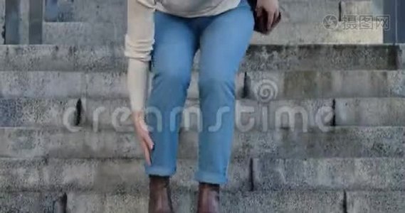 女性白种人的腿部特写，因为脚踝疼痛而走下楼梯并停止。 穿牛仔裤和棕色衣服的女人视频