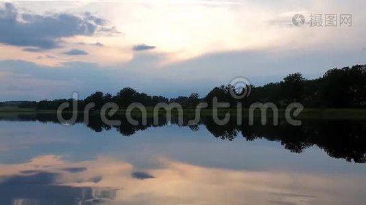 在平静的夏夜欣赏绚丽的日落。 湖岸有绿树和植物在晶莹洁净的镜面水中倒影..视频