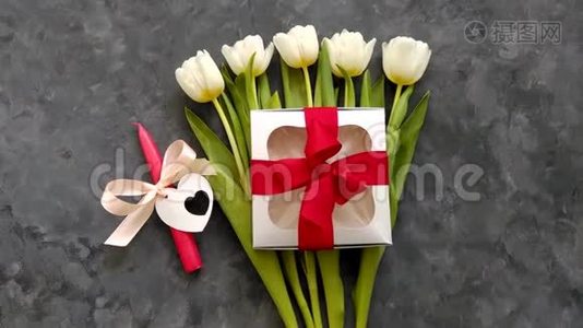 白色郁金香花，银色礼盒，红色丝带蝴蝶结和蜡烛在黑暗背景平躺4K顶部视图。 浪漫爱情视频