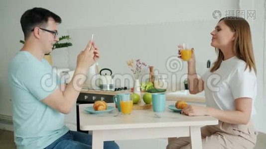 年轻女性摆着果汁的姿势，而丈夫则用智能手机拍照视频