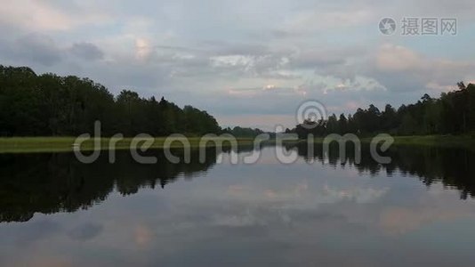 在平静的夏夜欣赏绚丽的日落。 湖岸上有绿树和植物，晶莹剔透的镜面水苏视频