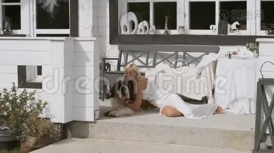 一个年轻的女孩抱着一只大狗，坐在房子附近的门廊上微笑。 总体计划视频