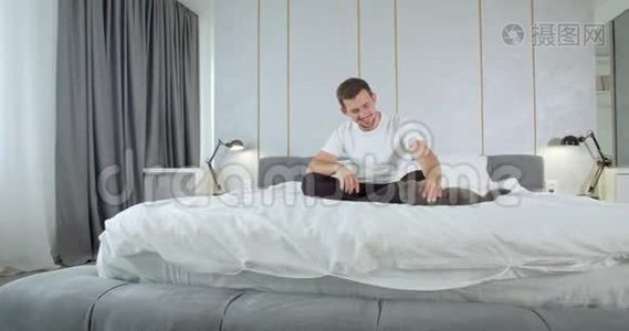 年轻人坐在床上抚摸他的猫，现代公寓，4K视频