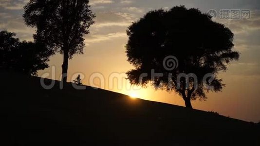 日落时骑自行车慢慢下山的小孩剪影视频