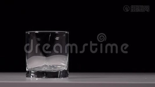 在黑色背景的白色桌子上，将水倒入透明玻璃的工作室镜头视频