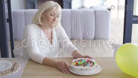 伤心的、不快乐的、成熟的女人坐在EMLPY房间的小生日蛋糕前的桌子旁，然后站起来走着视频